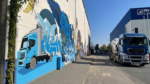 Eine lebendige Wandmalerei auf einem Gebäude mit einem blauen Lastwagen und verschiedenen abstrakten Motiven, neben dem ein blauer Lastwagen parkt.