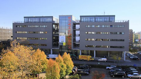 Ein modernes, mehrstöckiges Gebäude mit dem Logo "KONTORHAUS" an der Fassade. Das Gebäude ist von herbstlich gefärbten Bäumen umgeben, und im Vordergrund sind mehrere Fahrzeuge geparkt.