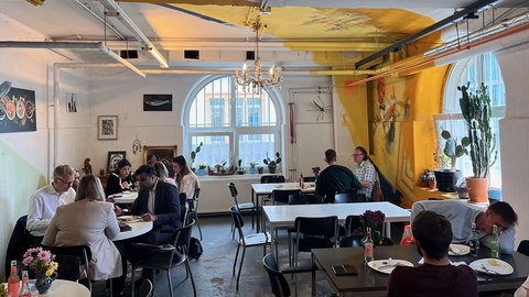 Ein modernes Café, in dem die Gäste an Tischen sitzen, ein Kronleuchter von der Decke hängt und Kunstwerke an den Wänden hängen.