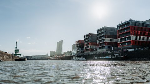 Eine moderne Stadtlandschaft am Osthafen mit Booten und einem hohen Gebäude unter einem klaren Himmel.