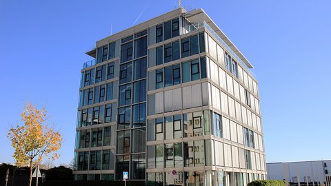 Ein modernes mehrstöckiges Gebäude mit einer Kombination aus Glas- und Betonfassaden vor einem strahlend blauen Himmel.