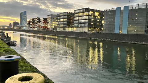Ein modernes städtisches Viertel im Frankfurter Osthafen mit mehrstöckigen Gebäuden, einem spiegelnden Hafenbecken und ein paar Booten.