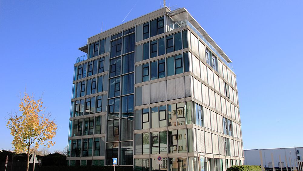 Ein modernes mehrstöckiges Gebäude mit einer Kombination aus Glas- und Betonfassaden vor einem strahlend blauen Himmel.